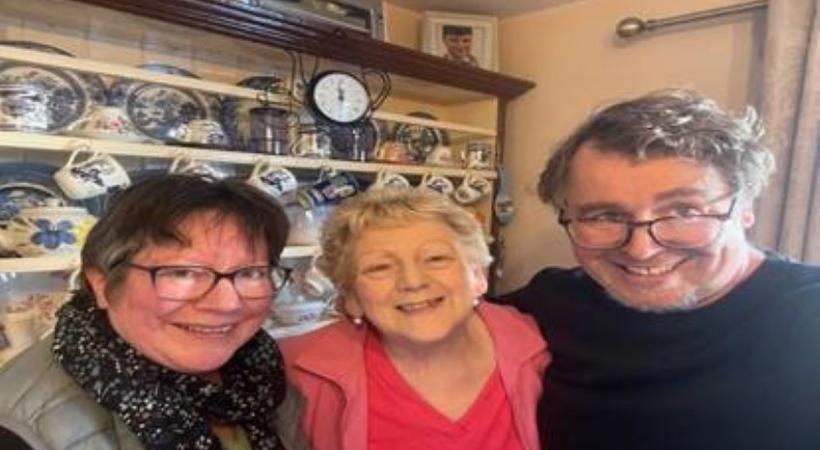 Two women and one man smiling in front of a dresser